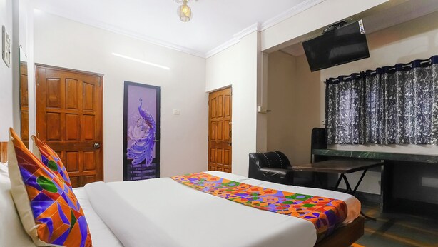 A hotel room with a bed, a desk, and a chair. There are two doors, one with a peacock design and another with a wooden panel. A TV is mounted on the wall above the desk. - Fabhotel Peaceful Studio Aai Bungalow (Panvel)