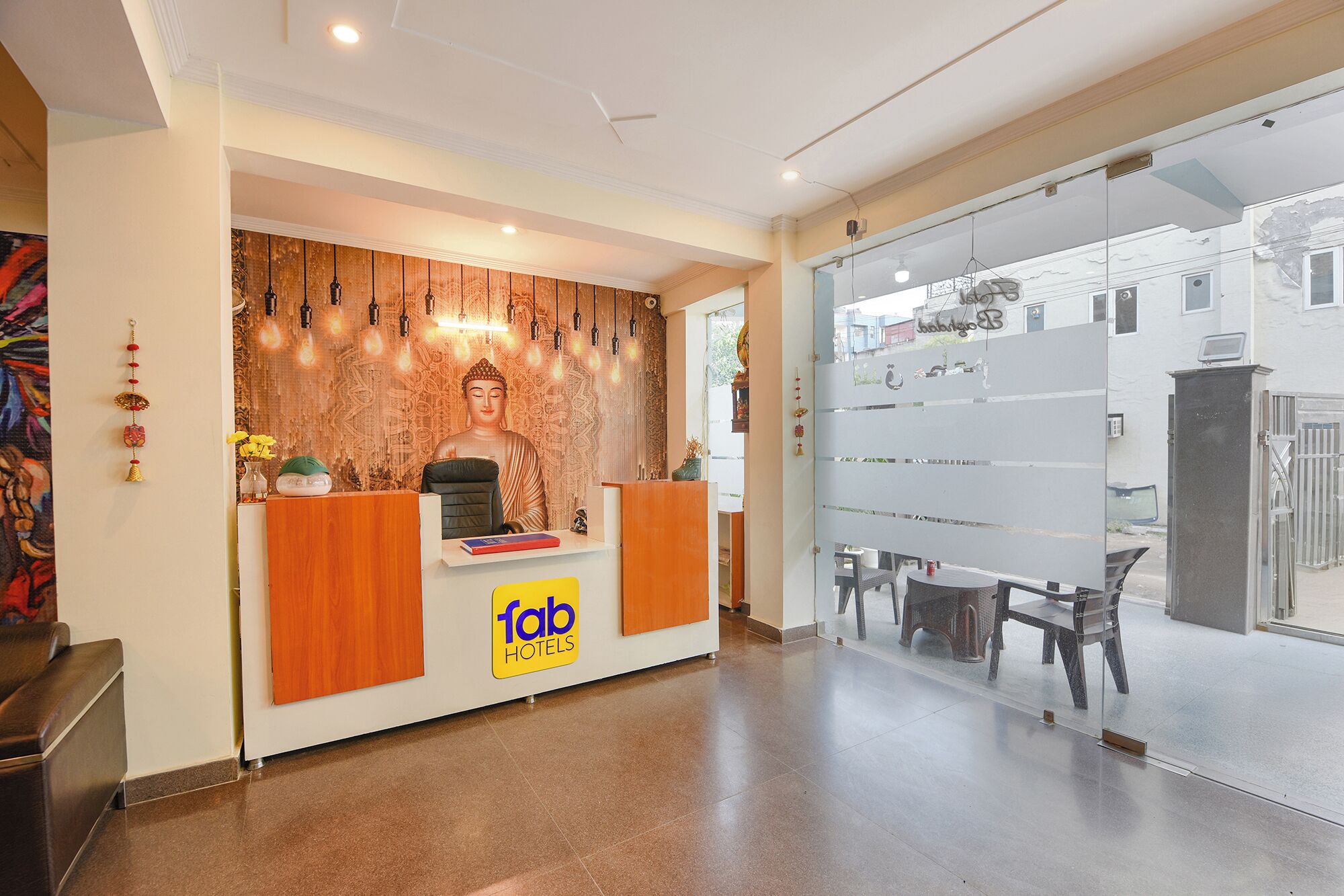 A hotel reception area with a Buddha statue, a reception desk, and a glass wall with a view of the street.