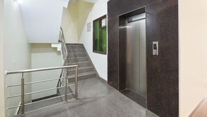 A modern elevator with a metallic finish, a staircase with a metal railing, and a wall with a dark marble-like texture. - Fabhotel The Flora (Gurugram)