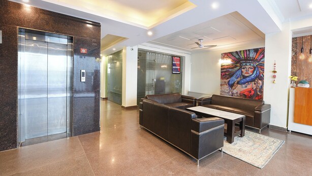 A lobby with a reception desk, seating area, elevators, and a mural. - Fabhotel The Flora (Gurugram)