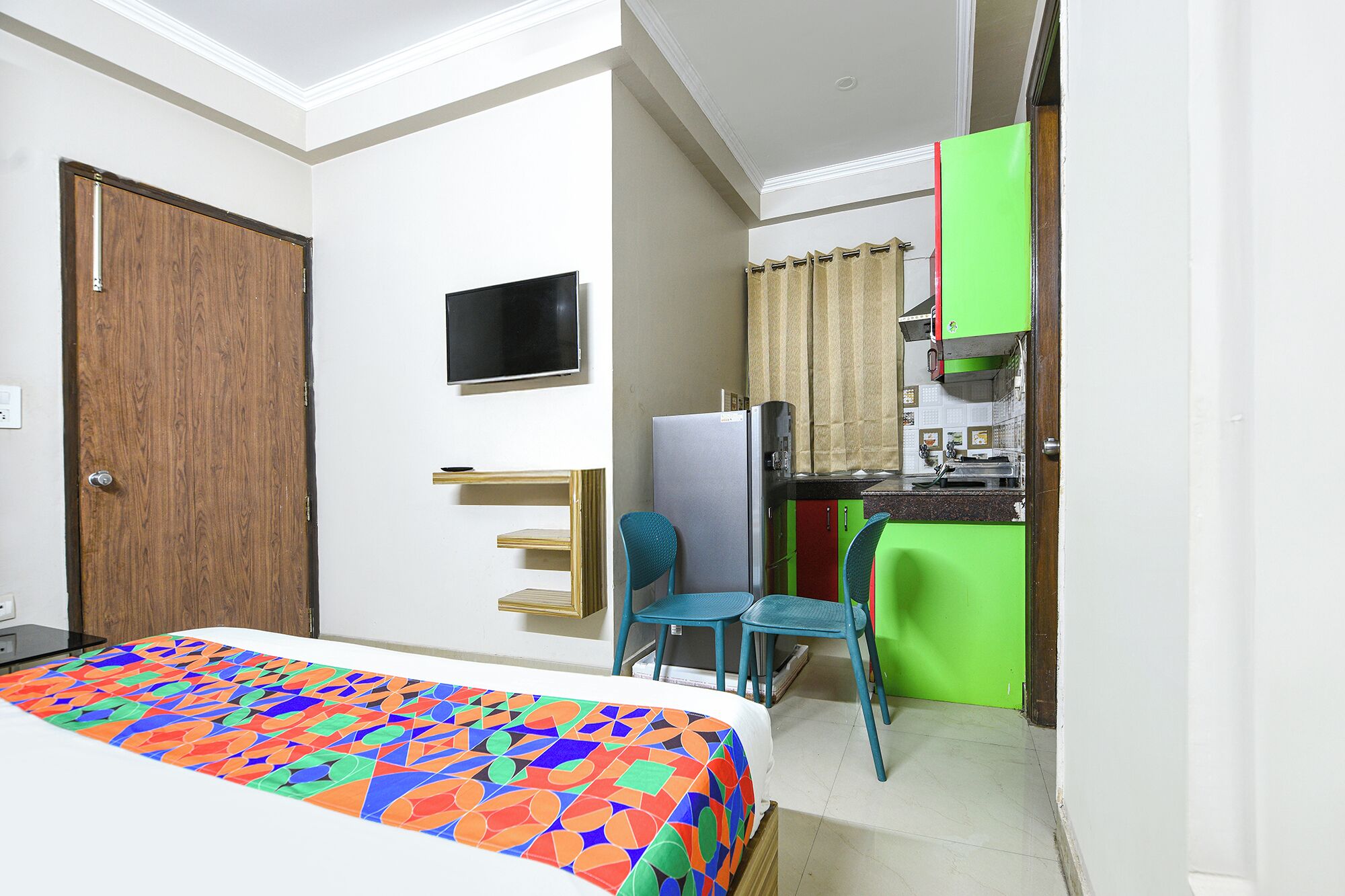 A bedroom with a bed, a TV, a desk, and a kitchenette.