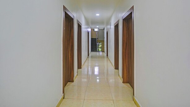 A long, narrow hallway with wooden doors on both sides and a tiled floor. - Fabhotel Ashiyana (Pune)