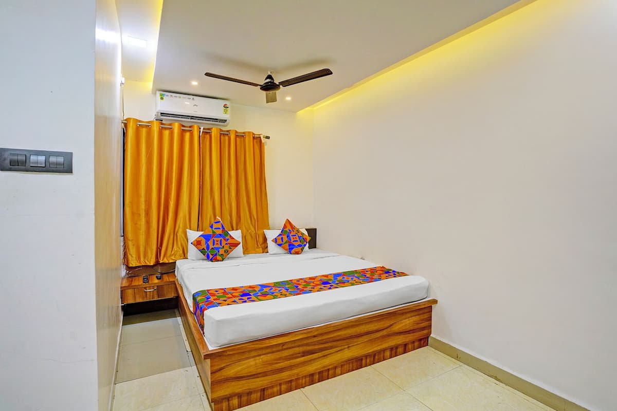 A bedroom with a wooden bed, a ceiling fan, an air conditioning unit, and a bathroom with a toilet and sink.