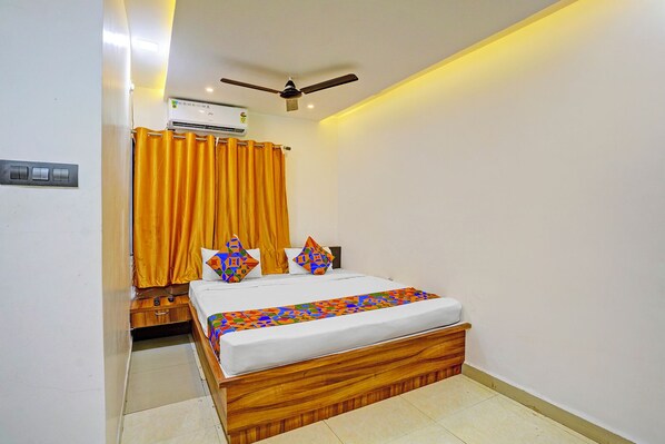 A bedroom with a wooden bed, a ceiling fan, an air conditioning unit, and a bathroom with a toilet and sink.
