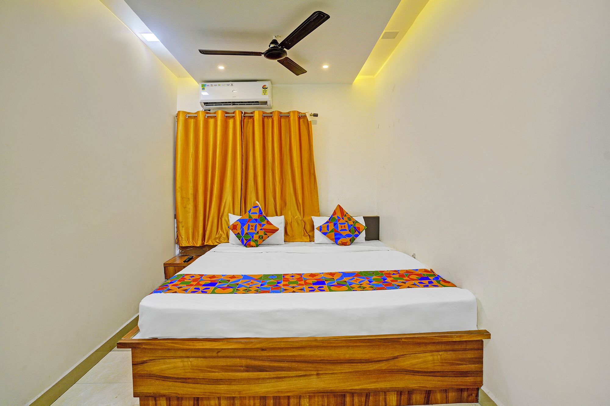 A bedroom with a wooden bed, a ceiling fan, an air conditioning unit, and yellow curtains.
