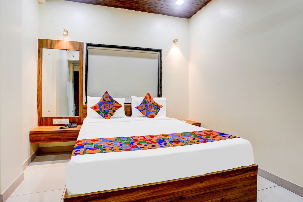 Habitación de hotel con estructura de cama de madera, un espejo grande y una colcha de diseño geométrico y colores vivos.
