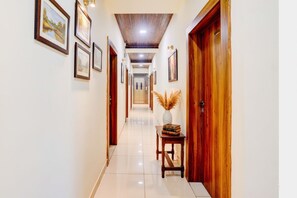 A hallway with framed pictures on the walls, a wooden door on the right, and a small table with a vase and books in the center. - Fabhotel The Royal Park (Pune)