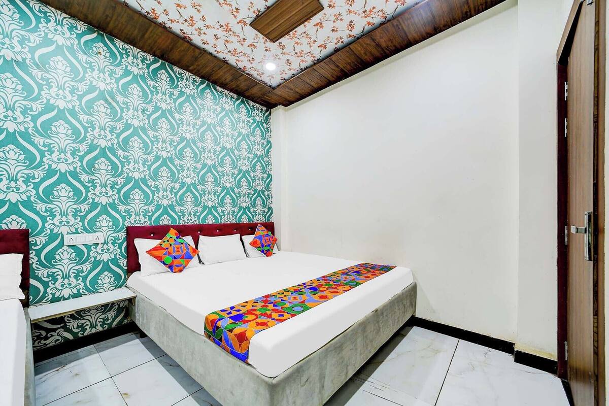 A bedroom with a bed, a nightstand, a patterned wall, and a wooden ceiling.