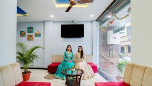 A modern living room with a ceiling fan, a flat-screen TV, and red sofas. - Fabhotel Mahak Palace (Ujjain)