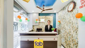 A hotel reception area with a modern design, a ceiling fan, a clock, and a reception desk with a logo. - Fabhotel Mahak Palace (Ujjain)