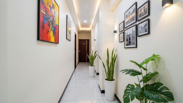 A hallway with a white tiled floor, potted plants, framed pictures on the walls, and a ceiling with recessed lighting. - Fabhotel Mahak Palace (Ujjain)