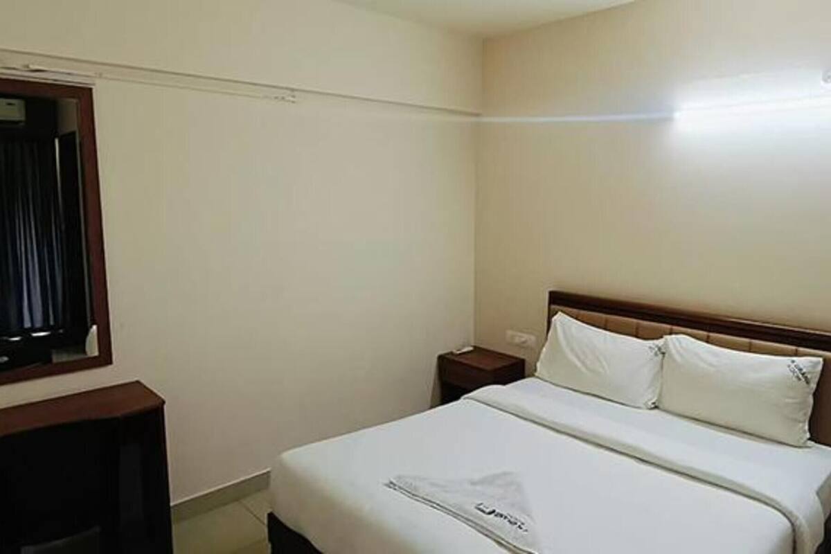 A hotel room with a single bed, a nightstand, a small table, and a window with curtains.