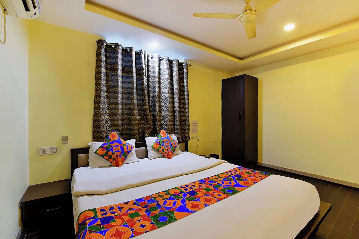 A hotel room with a bed, a ceiling fan, a dark-colored wardrobe, and patterned curtains.