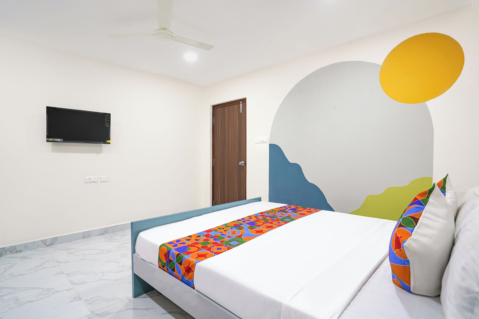 A bedroom with a bed, a TV mounted on the wall, and a door.