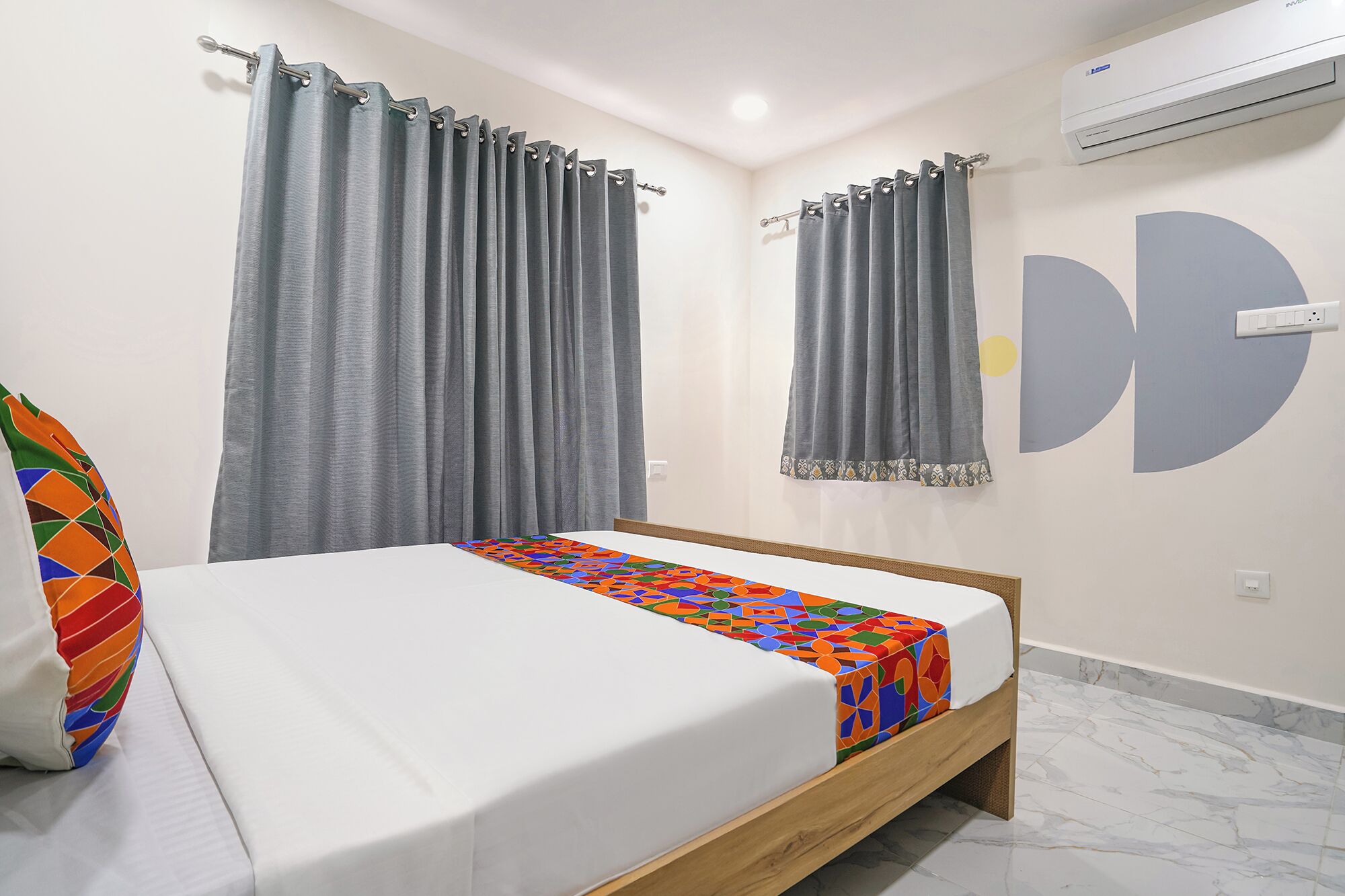 A bedroom with a bed, two curtains, a wall-mounted air conditioner, and a geometric wall decoration.