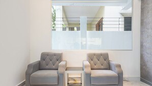 A modern room with two grey armchairs, a small white table, and a large window offering a view of the outside.