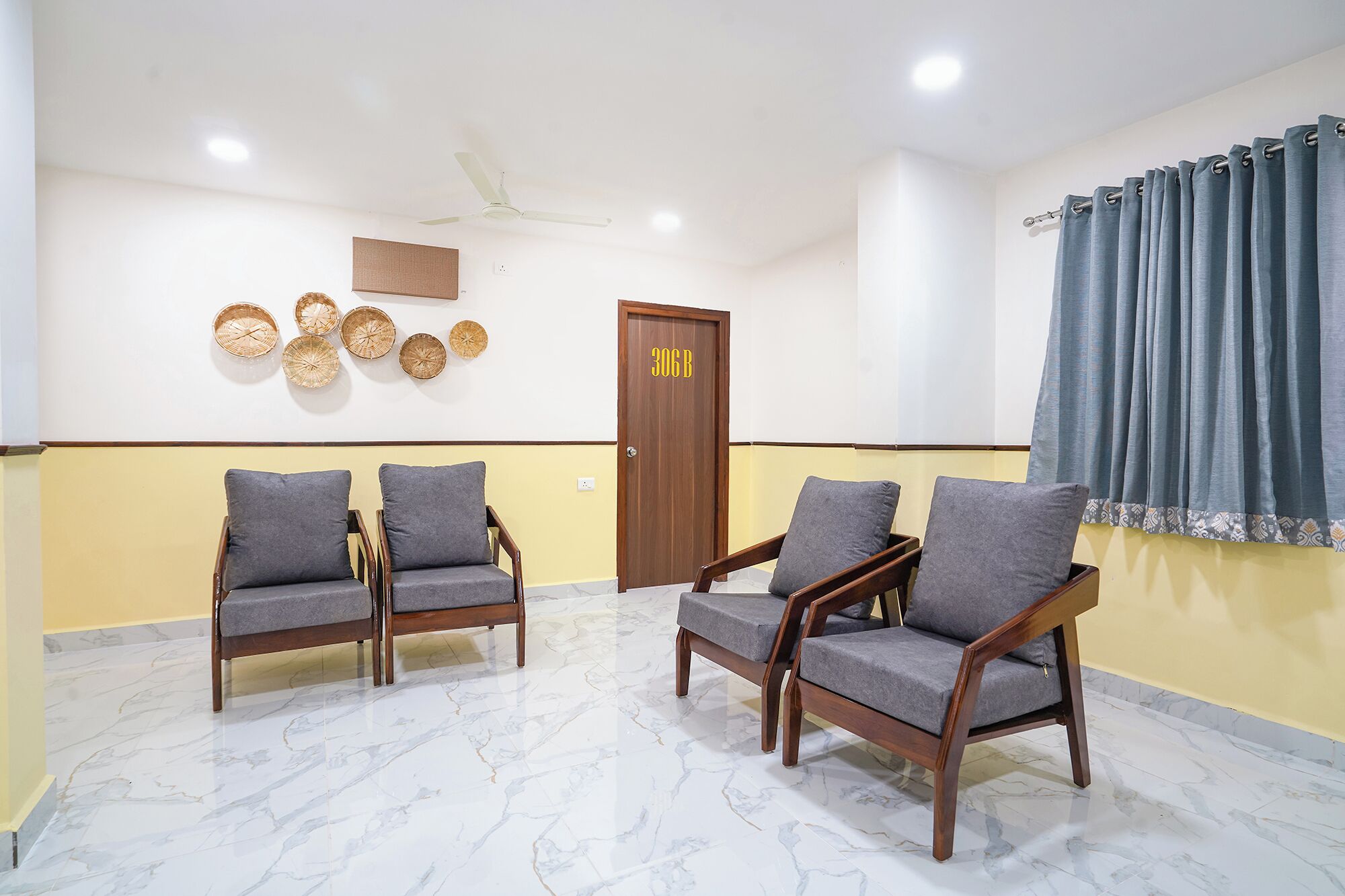 A waiting area with four wooden chairs, a door with a number, and a ceiling fan.