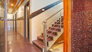 A modern interior with a polished marble staircase, a wooden ceiling, and a glass door leading to a hallway. - FabExpress Mount City Park (Bangalore)