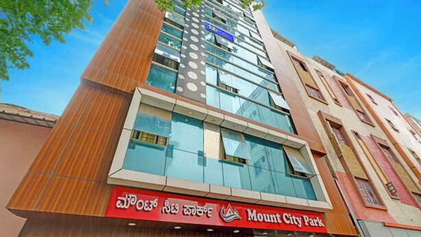 A modern hotel with a prominent 'Mount City Park' sign, featuring a mix of glass and wood facade, and a clear view of the sky. - FabExpress Mount City Park (Bangalore)