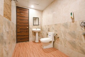 A bathroom with a wooden door, a pedestal sink, a toilet, and a mirror on the wall. - Hotel HSP Suites - Near IGI Airport - New Delhi (New Delhi)