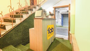 A hotel lobby with a wooden reception desk, a staircase with metal railings, and a door leading outside. - Fabhotel City Palace (Kolkata)