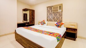A hotel room with a large bed, a wooden wardrobe, a mirror, a window with patterned curtains, and a bedside table. - Fabhotel Travellers (Lucknow)