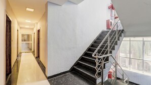 A modern hotel interior with a marble-floored corridor leading to a staircase with metal railings and a red fire extinguisher mounted on the wall. - Fabhotel Travellers (Lucknow)