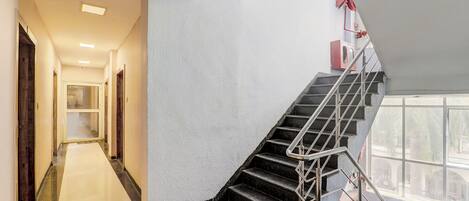 A modern hotel interior with a marble-floored corridor leading to a staircase with metal railings and a red fire extinguisher mounted on the wall.