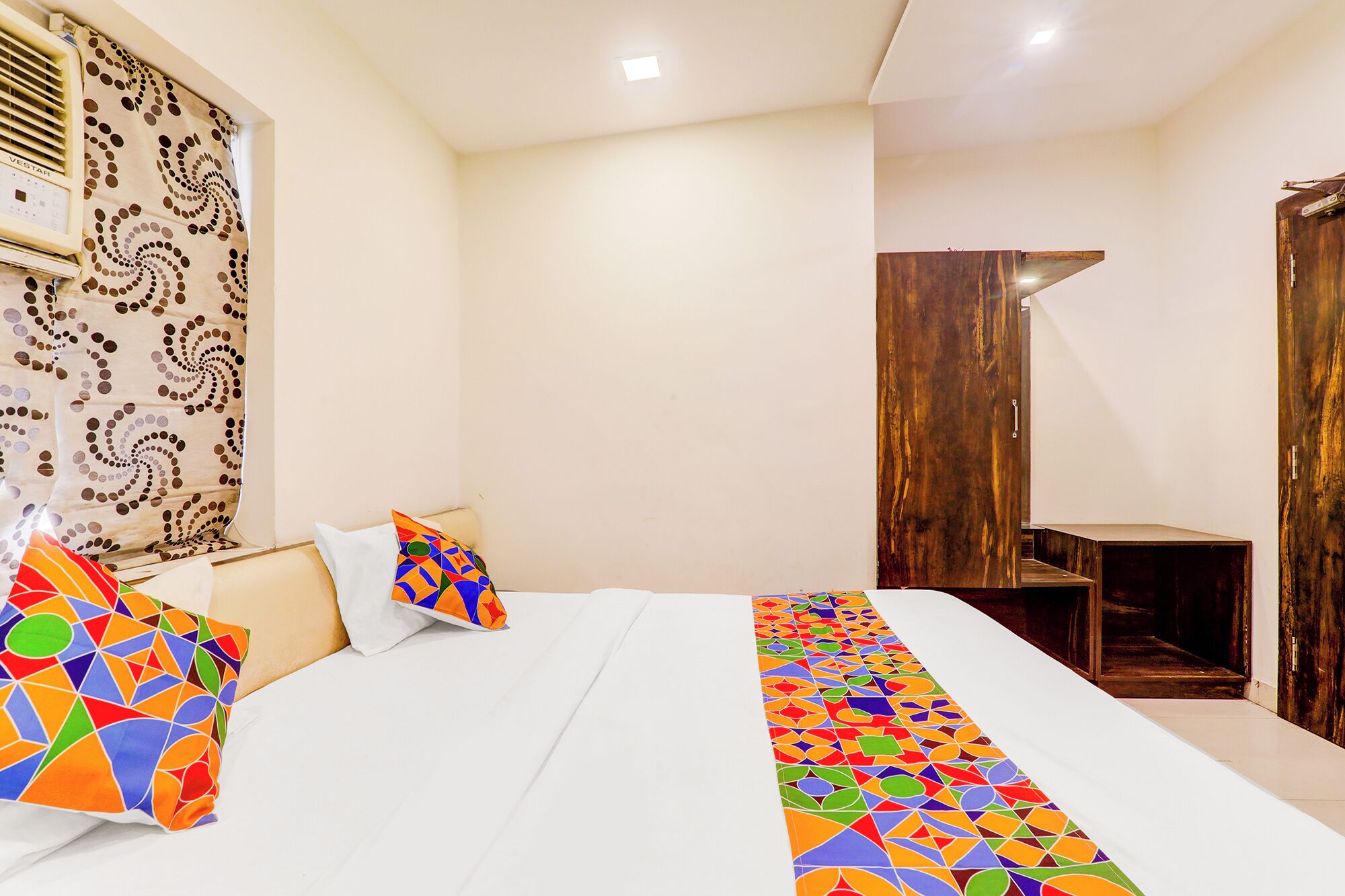A hotel room with a bed, a wooden wardrobe, and a patterned curtain.