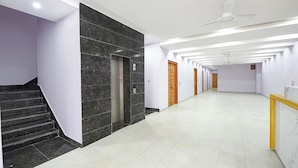 A modern hallway with a marble staircase, elevators, and a ceiling fan. - FabHotel Naveen Stay (Gurugram)