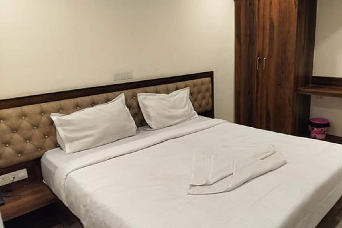 Una cama bien hecha con un cabecero capitonado, un armario de madera y un pequeño recipiente rosa en el suelo.