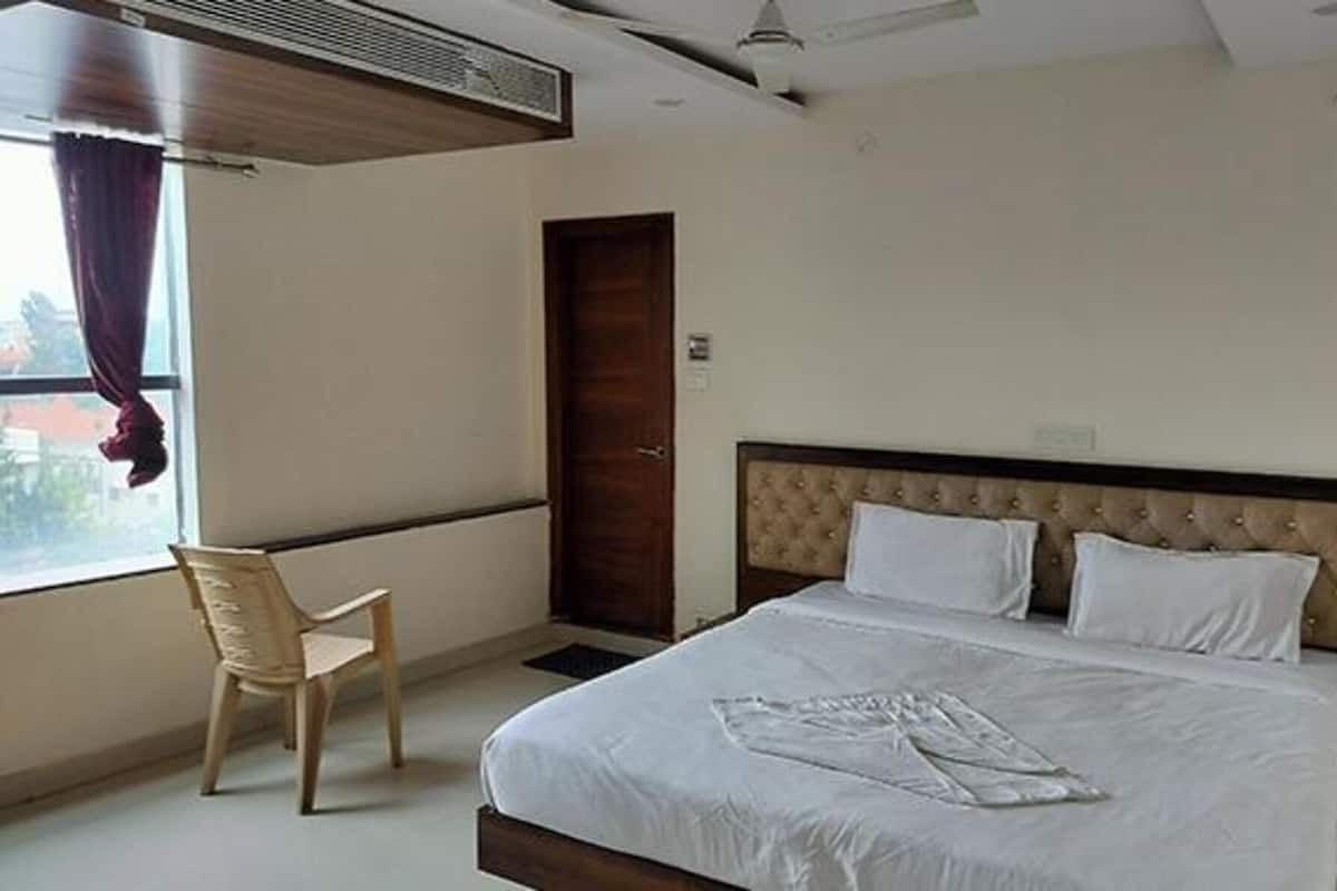 Habitación de hotel con una cama grande, un cabecero de madera, una silla y una ventana con cortinas.