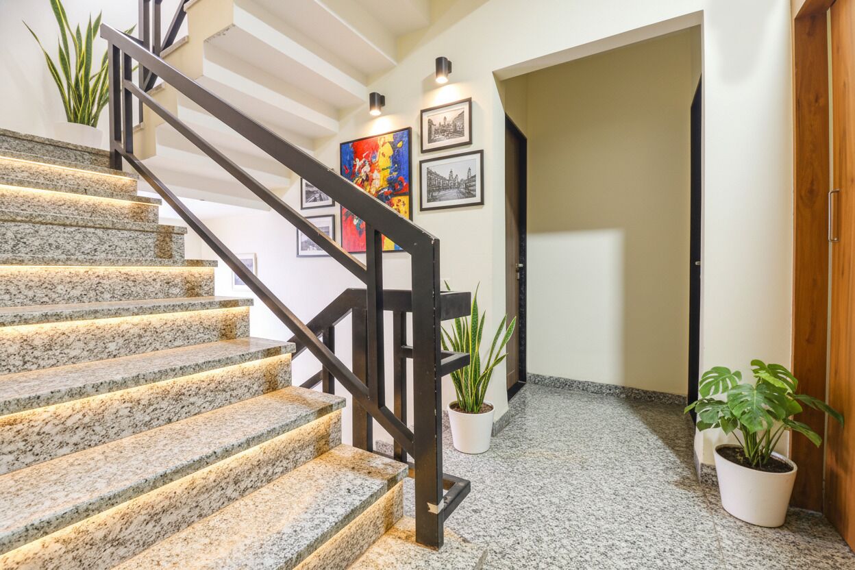 Una escalera con escalones de granito y barandilla de metal negro, que conduce a una habitación con puerta de madera.