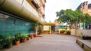 A courtyard with potted plants, a covered seating area, and a building with a green facade. - Fabhotel Panchratna (Panvel)