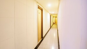 A long, narrow hotel corridor with white tiled walls and a tiled floor. - Fabhotel Panchratna (Panvel)