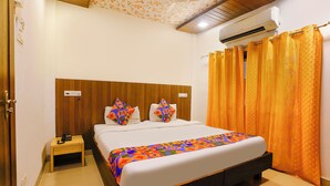 A neatly arranged bedroom with a wooden headboard, a bed with colorful bedding, a bedside table, and an air conditioning unit on the wall. - Fabhotel Panchratna (Panvel)