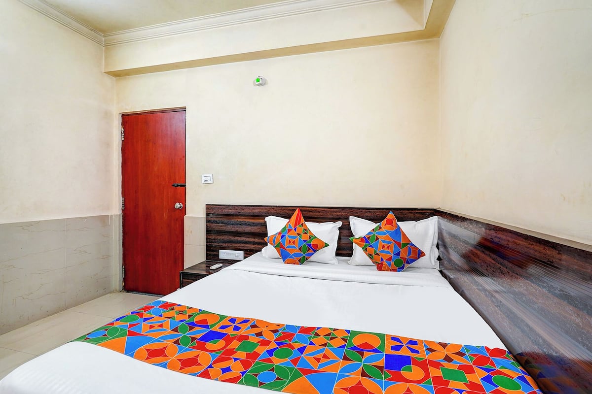A hotel room with a wooden headboard, a bed with a colorful geometric-patterned bedspread, and a red door.