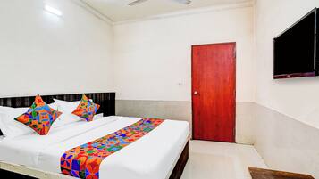 A hotel room with a bed, a ceiling fan, a wooden door, and a TV mounted on the wall.