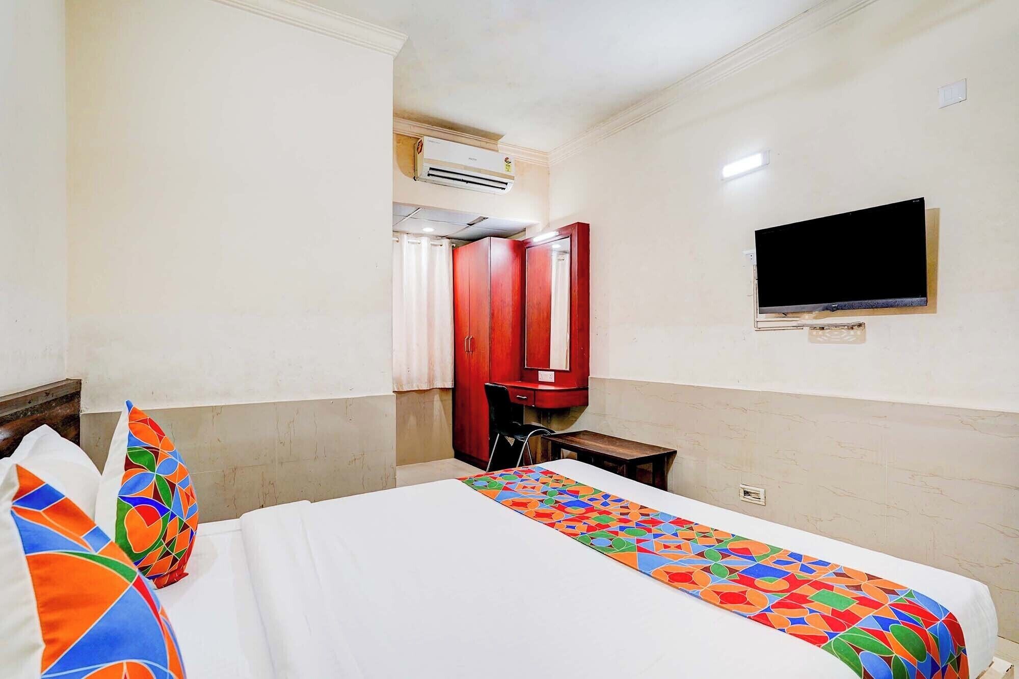 A hotel room with a bed, a TV, a wardrobe, and an air conditioning unit.