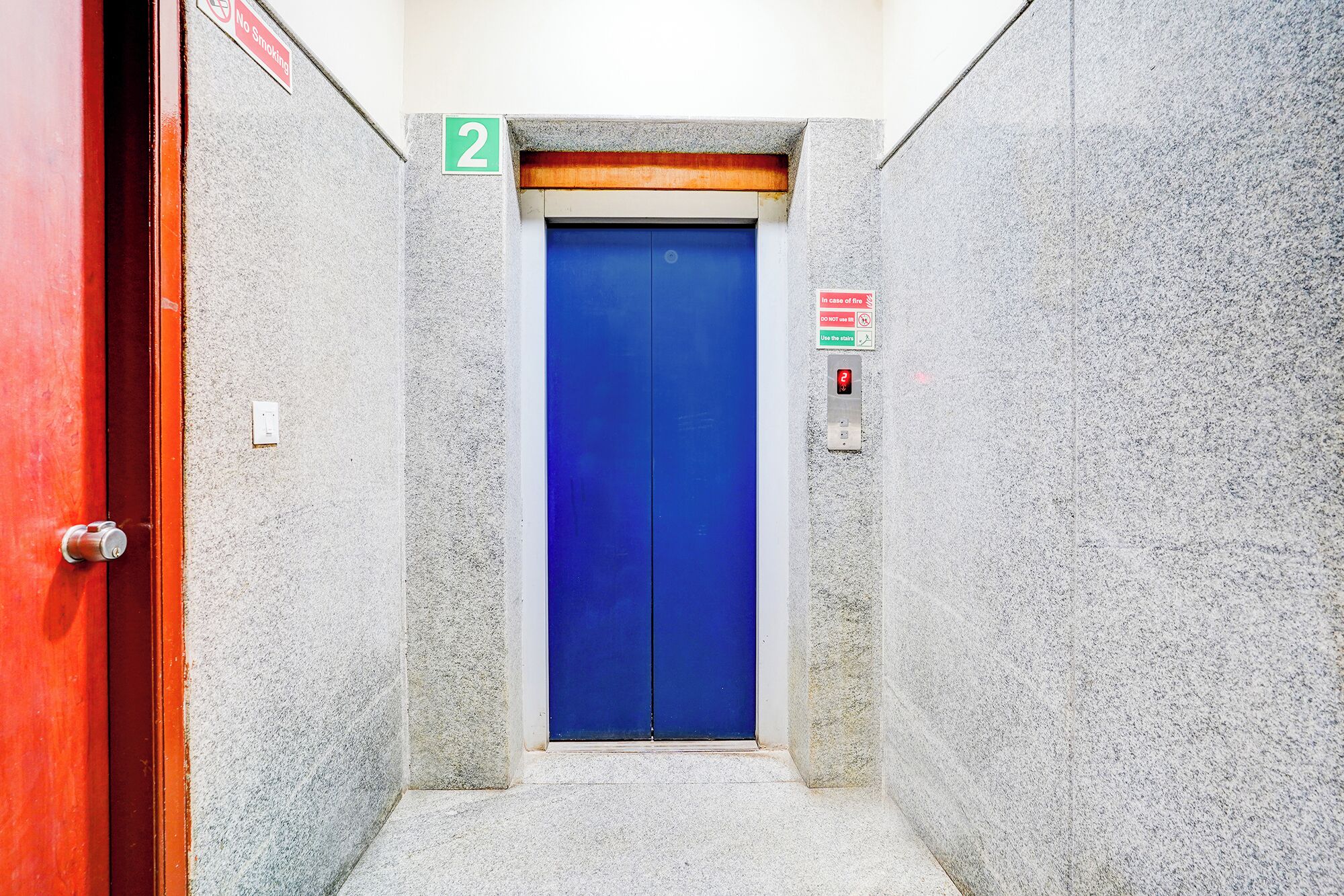 Un couloir étroit avec une porte bleue, une porte rouge sur la gauche et un panneau « Il est interdit de fumer » au-dessus de la porte.