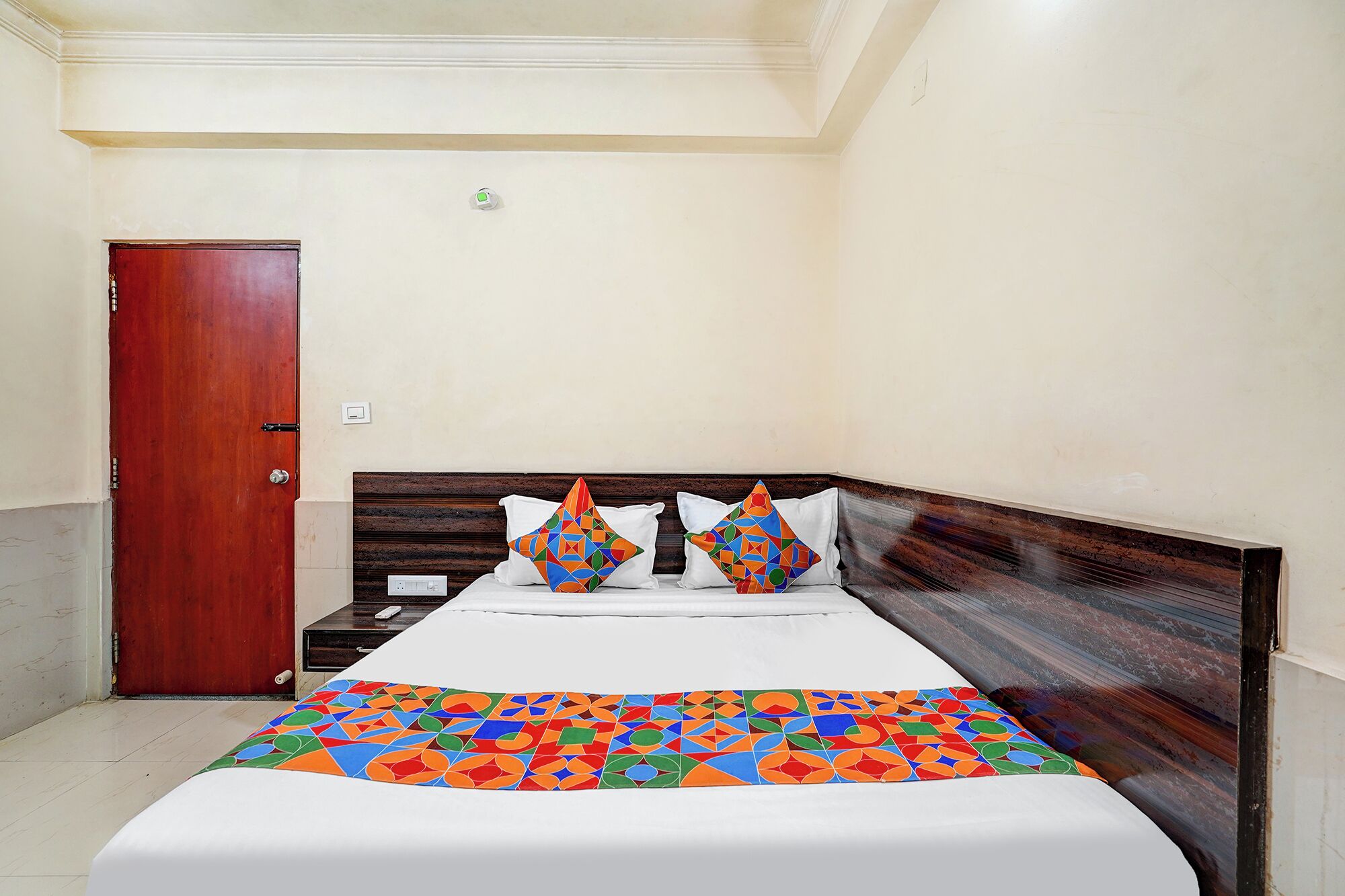 Ein Hotelzimmer mit einem hölzernen Kopfteil, einer weißen Bettdecke und zwei farbenfrohen geometrischen Kissen.