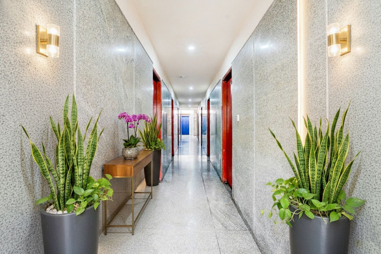 A hallway with a polished granite floor, potted plants, a wooden bench, and red doors.