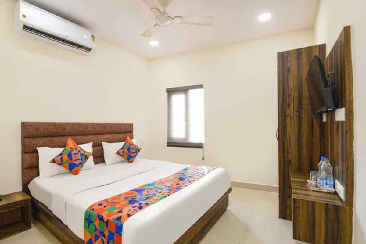 A hotel room with a bed, a ceiling fan, an air conditioner, a window, and a wooden wardrobe with a TV.