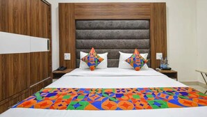 Habitació d'hotel amb armari de fusta, un llit amb llençol estampat de motius geomètrics i un capçal de llit amb panells horitzontals.
