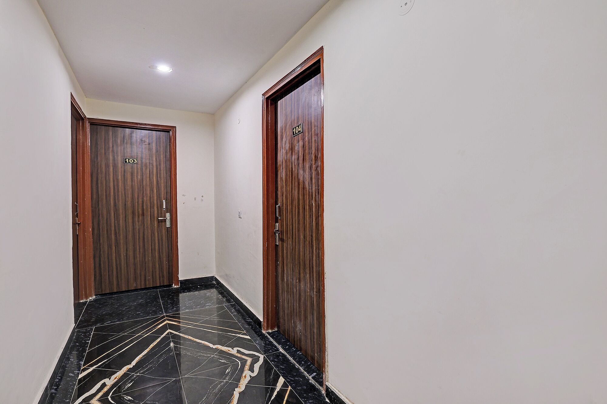 A hallway with two wooden doors, numbered 103 and 104, and a black marble floor with a geometric pattern.