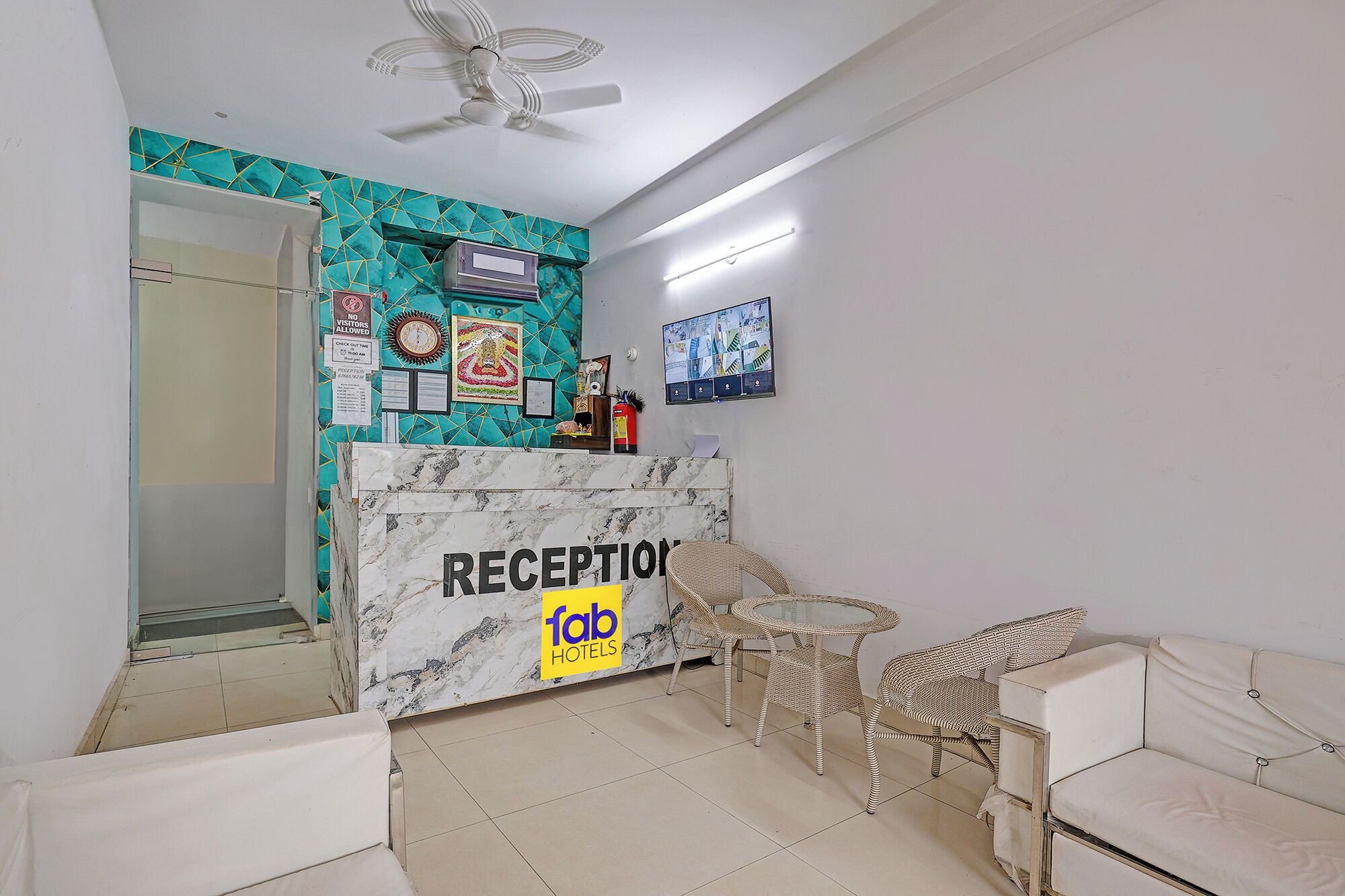 Zona de recepción con mostrador de mármol, mobiliario de mimbre y un ventilador de techo.