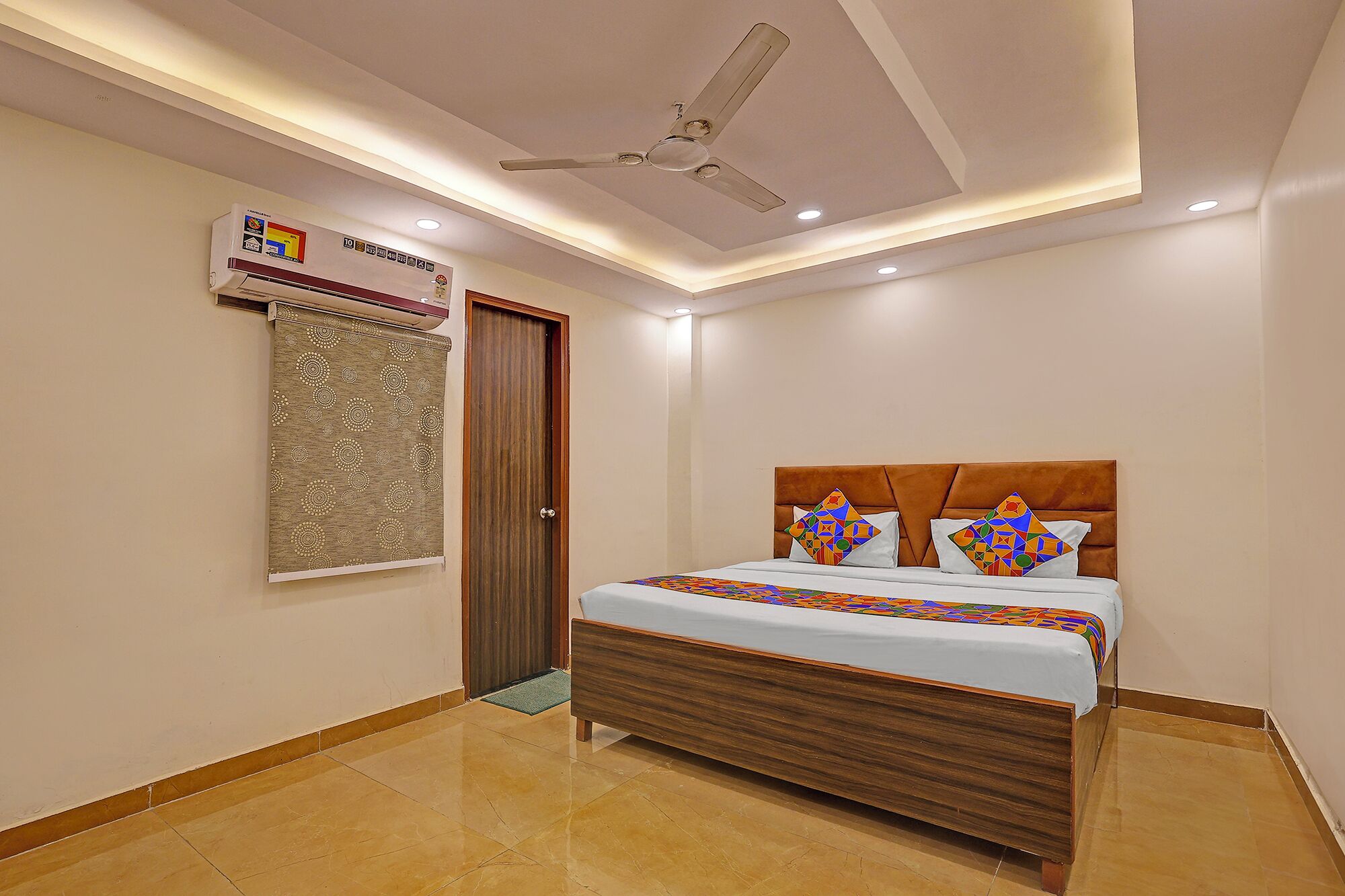 A hotel room with a bed, a ceiling fan, an air conditioning unit, and a patterned curtain.