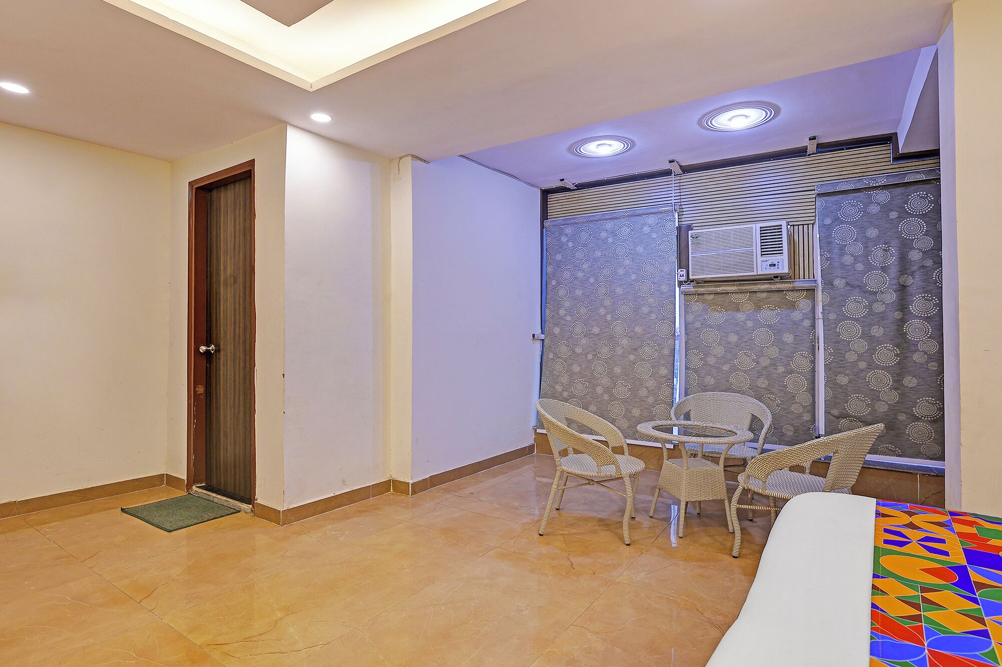 Una habitación pequeña y bien iluminada, con piso de baldosas, una puerta, una mesa pequeña con sillas y un papel tapiz decorado.