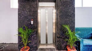 An elevator with a digital display showing the number 2, flanked by two potted plants, in a lobby with a teal sofa. - Fabhotel Aashvi (Hyderabad)