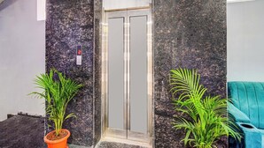 An elevator with a digital display, flanked by dark marble walls and potted plants. - Fabhotel Aashvi (Hyderabad)